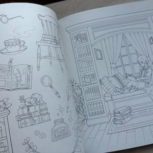 Pu&ograve; includere: Pagina di un libro da colorare aperto con un disegno a tratto dettagliato. L'illustrazione presenta un angolo lettura accogliente con una persona che legge, circondata da librerie, libri ed elementi decorativi come fiori, una tazza di t&egrave; e una lente d'ingrandimento.