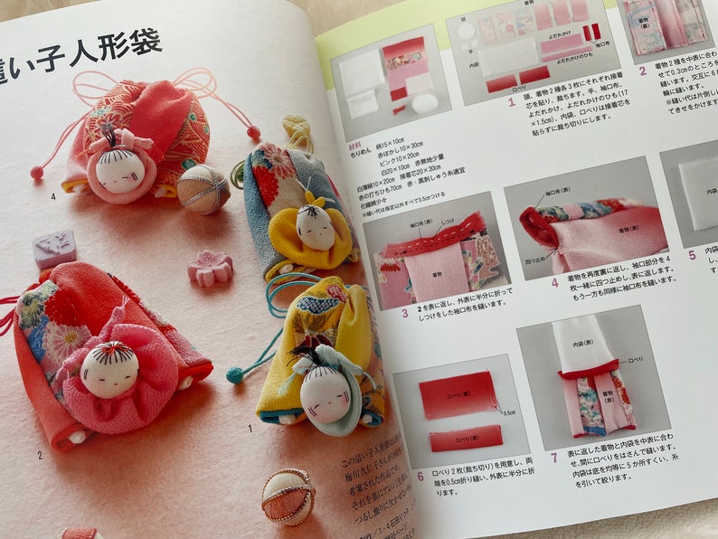 May include: A close-up of three handmade fabric dolls with colorful kimono-style outfits. The dolls are sitting on a pink surface with a white background. The dolls are about 3 inches tall and have black eyes and red lips. The dolls are wearing traditional Japanese clothing.