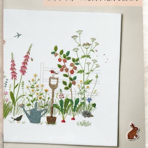 May include: A book cover with a white background and a colorful embroidered image of a garden scene. The title of the book is "Cotswolds and Lake District" and the author is "青木和子".