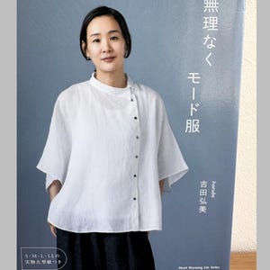 Puede incluir: Una mujer con una blusa blanca y una falda oscura está de pie junto a un libro. La portada del libro tiene texto japonés y el título "Mode Clothes". El libro también tiene el texto "S, M, L, LL".