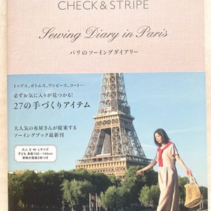Puede incluir: Una portada de libro con fondo rosa y el título "Sewing Diary in Paris" en letra cursiva negra. El libro presenta una foto de la Torre Eiffel y una mujer que lleva un vestido rosa claro y camina hacia la cámara. El libro se titula "Sewing Diary in Paris" y tiene el subtítulo "Diario de costura de París". La portada del libro también incluye el texto "Check & Stripe" y "27 artículos hechos a mano".