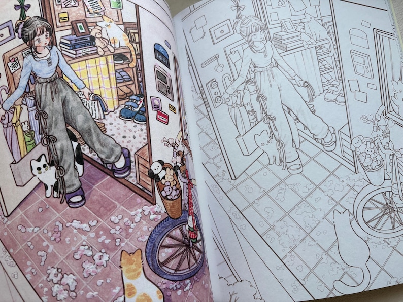 May include: An open colouring book displaying two pages with an anime-style illustration of a person in a light blue long-sleeve shirt and dark grey trousers standing in a room with a bicycle, cats, and various household items in both colour and line art.