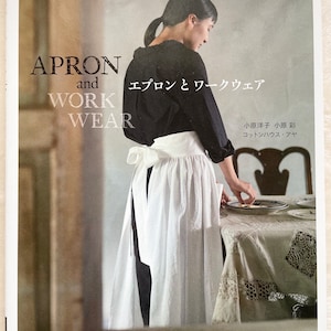 May include: A book cover featuring a woman wearing a white apron and a black shirt. The book title is "Apron and Work Wear" with the text "エプロンとワークウェア" in Japanese. The book is by 小原洋子 小原彩 and コットンハウス・アヤ. The book cover also includes the text "縫い代つき実物大パターン2枚" and "文化出版局".