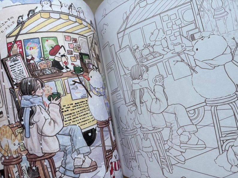 May include: A colouring book open to two pages showing a winter scene with a food truck, a person sitting on a stool holding a mug, a snowman, and a cat. The left page is coloured in soft tones, while the right page features the same line art illustration.