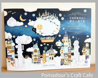 May include: A coloring book with a dark blue night sky cover featuring white clouds, a crescent moon, stars, and a hot air balloon carrying a small town. The text reads "空想街雑貨店の夢見る塗り絵" and "KUUSOOGAI'S DREAMY COLORING BOOK" with intricate building illustrations.