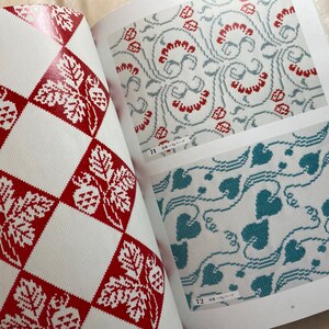 May include: A book with three different cross-stitch patterns. The first pattern is a red and white checkered pattern with a leaf and berry design. The second pattern is a light blue and white pattern with a floral design. The third pattern is a teal and white pattern with a leaf design.