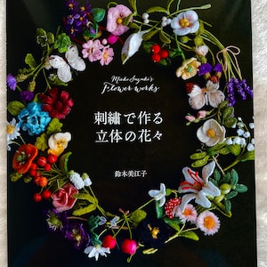 May include: Book cover featuring a wreath of embroidered flowers in various colors, including red, white, pink, purple, and green. The title of the book is "Embroidered Flowers" in Japanese characters. The author's name is "Mieko Suzuki" and the publisher is "Bunka Publishing Co."