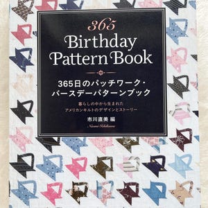 Könnte beinhalten: Ein Buch mit dem Titel "365 Birthday Pattern Book" mit schwarzem Einband und weißem Text. Das Buch zeigt im Hintergrund ein farbenfrohes Patchwork-Design. Der Text im Bild enthält auch japanische Schriftzeichen.