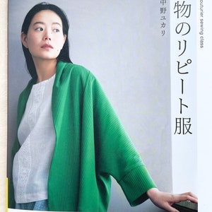 May include: A book cover featuring a woman wearing a green ribbed cardigan and a white lace top. The book title is "Real Fabric Repeats" and the subtitle is "Couturier Sewing Class". The book is published by "Heart Warming Life Series" and "The Japanese Vogue Company".