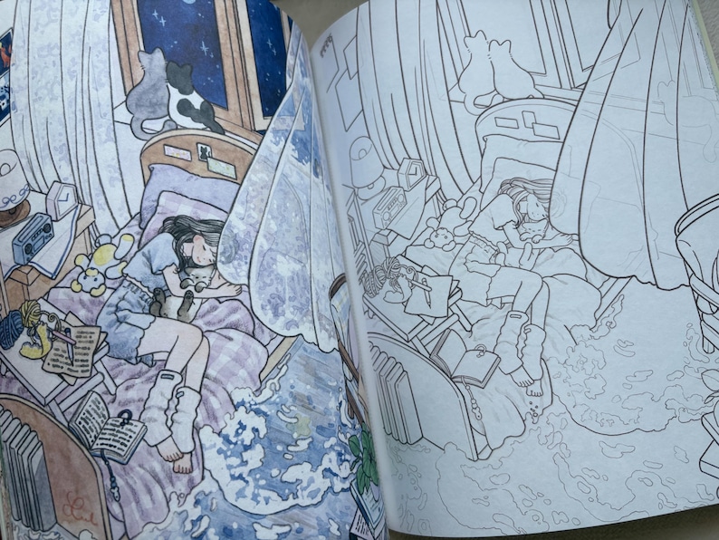 May include: An open colouring book featuring two side-by-side illustrations of a bedroom scene. One page is coloured with soft tones showing a person sleeping with a cat on a bed, while the other page displays the same scene in black and white line art.