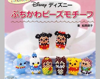 May include: A craft book cover featuring a white teacup and eight small, colourful Disney character figures made from tiny beads. The Japanese text includes the title "Disney" and "Puchikawa Beads Motif" with author credit to Matsuoka Akiko.