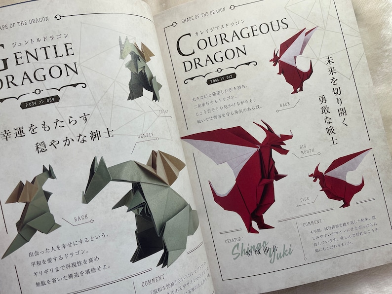 May include: Two origami dragons, one red and one green, are shown folded in different poses. The red dragon is labeled "Courageous Dragon" and the green dragon is labeled "Gentle Dragon". The book page features Japanese text and illustrations.