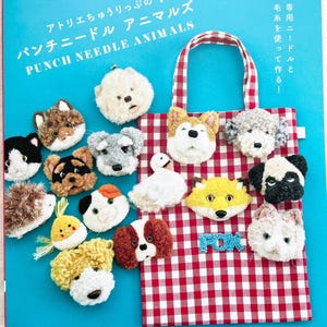 Op de afbeelding: Een boekomslag met een blauwe achtergrond en een rode en witte geruite draagtas. De titel van het boek is "Punch Needle Animals" en de omslag toont verschillende dierlijke vormen gemaakt met naaldvilten.