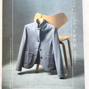 Puede incluir: Una portada de libro con una chaqueta gris sobre una silla de madera. El título del libro es "20 Jackets Pomadour's" y el texto "Chaquetas geniales para hacer" está en el lado derecho de la portada.