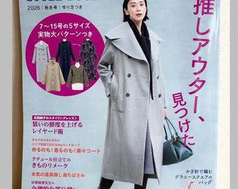 May include: A Japanese fashion magazine titled Style Book 2026 Autumn/Winter edition. The cover features a person wearing a long light gray double-breasted coat with a wide collar, black boots, and a dark handbag, alongside various garment patterns.