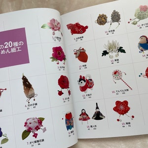 May include: A book with a pink cover featuring 20 different types of Japanese crafts made with fabric. The crafts are displayed in a grid format with a Japanese name and number for each craft. The book title is "Popular 20 Types of Chirimen Crafts".