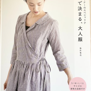 Può includere: Una copertina di libro con una donna che indossa un abito avvolgente a righe. Il titolo del libro è "Abito intero, Abbigliamento per adulti" e il testo "Specialità del designer" è anche visibile. La copertina del libro è bianca con testo nero.