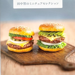 May include: Two miniature cheeseburgers on a wooden cutting board. The cheeseburgers are made of polymer clay and are very realistic. The cheeseburger on the left has lettuce, tomato, onion, and cheese. The cheeseburger on the right has lettuce, avocado, and cheese. The text "Pommadour's Craft Cafe" is at the bottom of the image.