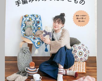 May include: A Japanese craft book titled "おうちでぬくぬく♪ 手編みのあったかこもの" featuring various hand-knitted and crocheted items including a blue floral blanket, a gray cable-knit hot water bottle cover, slippers, a tea cozy, and patterned socks.