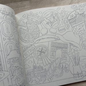 以下が含まれることがあります： 開いた塗り絵のページ。エッフェル塔、凱旋門、風車など、パリのシーンの詳細な線画。ワイングラス、マカロン、テディベアなどのイラストも含まれています。ページは複雑なデザインでいっぱいです。