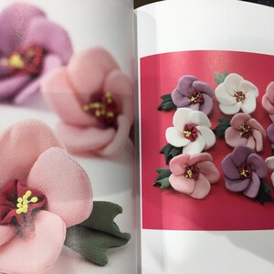 May include: A book open to a page showing a variety of fabric flowers in pink, white, and purple. The flowers are arranged in a circle on a red background.