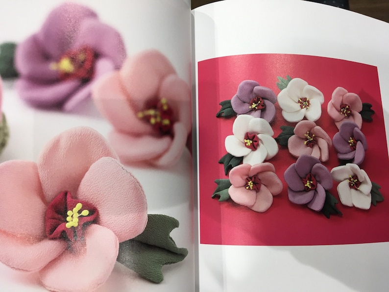 May include: A book open to a page showing a variety of fabric flowers in pink, white, and purple. The flowers are arranged in a circle on a red background.