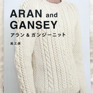 May include: A book cover featuring a white knitted sweater with a cable knit pattern. The title of the book is "ARAN and GANSEY" with the Japanese translation "アラン&ガンジーニット" below. The book is published by "風工房" and "文化出版局" and the bottom of the cover reads "Pomadour's Craft Cafe".