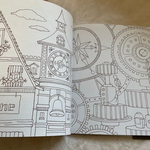 Puede incluir: Libro para colorear abierto con ilustraciones detalladas en l&iacute;nea. Una p&aacute;gina muestra un edificio con una torre de reloj, el nombre "Pauline" en un letrero y detalles florales. La otra p&aacute;gina representa engranajes, una rosa de los vientos y elementos mec&aacute;nicos.