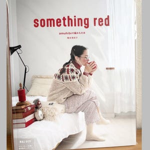 Peut inclure: Couverture de livre avec le titre "something red" en rouge. L'image montre une femme portant des lunettes et un pull, tenant une tasse rouge. Du texte japonais est également visible. La femme est assise sur un lit avec une couverture blanche.