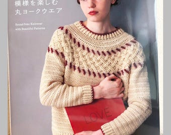 May include: A craft book cover titled applemints featuring a beige long-sleeve crochet sweater with a round yoke, intricate cable-like patterns, and dark red trim at the neckline, cuffs, and hem. The cover includes the text Round-Yoke Knitwear with Beautiful Patterns and the word LOVE on a red object.