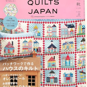 Può includere: Una copertina di rivista per Quilts Japan, una pubblicazione per quilter. La copertina presenta una trapunta fatta di case colorate con accenti rossi, bianchi e blu. Il titolo della rivista è in grandi caratteri grassetto e il testo "My Sweet House" è presentato in un carattere più piccolo. La copertina include anche il testo "Patchwork per realizzare una trapunta a forma di casa".