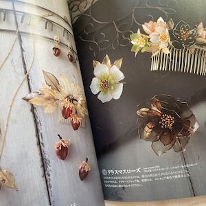 May include: A set of handmade jewelry featuring a gold chain necklace with a brown acorn pendant, a pair of earrings with brown acorn pendants, and a gold hair comb with brown acorn and white flower accents. The jewelry is displayed on a white wooden surface.