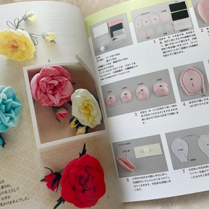 May include: A book with instructions on how to make fabric roses. The book shows different colored roses, including pink, blue, white, and red. The book also shows the steps involved in making the roses.