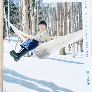 Puede incluir: Un libro titulado "Miknits" con el texto "Lo mejor de Miknits 2012-2018" y "Mariko Mikuni" en la portada. La portada presenta a un joven sentado en una hamaca en un bosque nevado.