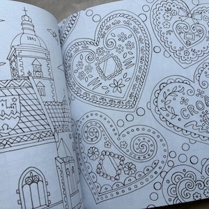 May include: An open coloring book page featuring detailed line drawings. One page depicts a church with a steeple and the year 1841. The other page showcases several heart-shaped designs with floral and decorative patterns, including the word "CROATIA".