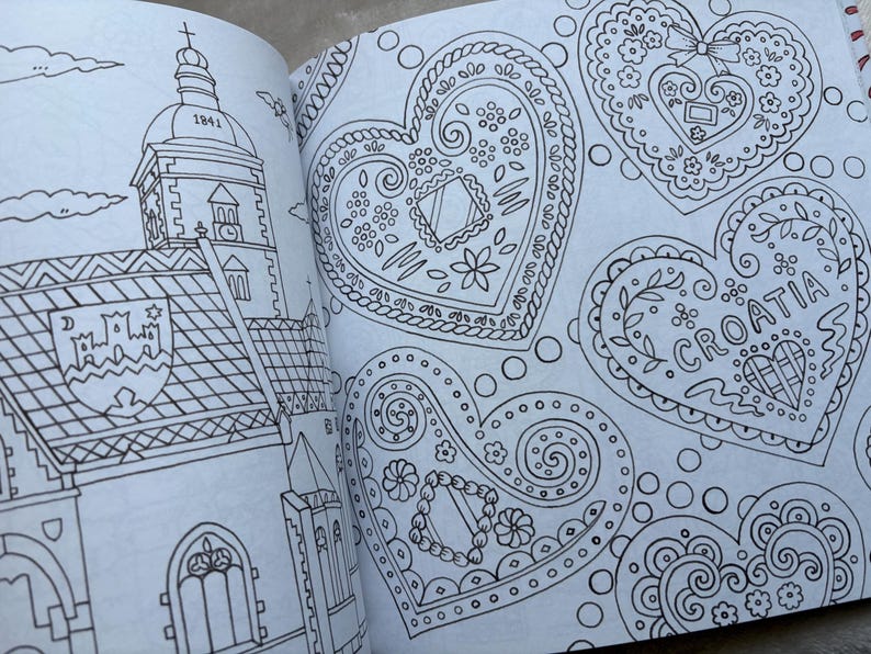 May include: An open coloring book page featuring detailed line drawings. One page depicts a church with a steeple and the year 1841. The other page showcases several heart-shaped designs with floral and decorative patterns, including the word "CROATIA".