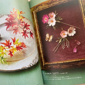 May include: Two pages from a book showing how to make hair accessories. The left page shows a white plate with a silver rabbit figurine and a comb with red, yellow, and orange leaves. The right page shows a framed picture with a burgundy background and three floral hair pins with pink and white flowers and a butterfly.