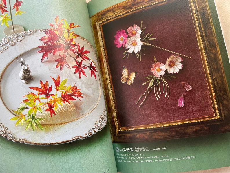 May include: Two pages from a book showing how to make hair accessories. The left page shows a white plate with a silver rabbit figurine and a comb with red, yellow, and orange leaves. The right page shows a framed picture with a burgundy background and three floral hair pins with pink and white flowers and a butterfly.