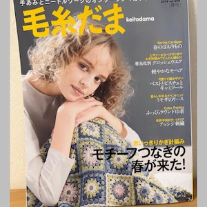 May include: A magazine cover featuring a woman with curly hair, holding a colorful crocheted blanket. The magazine title is "Keitodama" with Japanese text. The cover also includes text about knitting projects and a "Let's knit series" label.