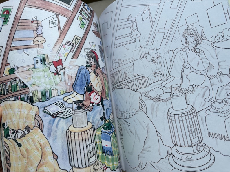 May include: A colouring book spread featuring two side-by-side illustrations of an attic room. One side is coloured with warm tones, showing a person sitting on a bed with a book, a heater, and a cat. The other side is a black and white line drawing.