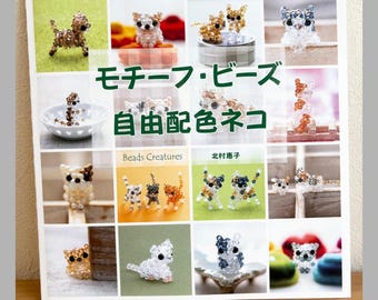 May include: A craft book cover titled "モチーフ・ビーズ 自由配色ネコ" featuring a grid of photographs displaying various small cat figurines constructed from colorful, translucent, and opaque beads in diverse poses and color combinations.