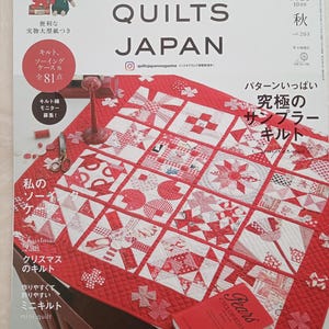 May include: The cover of "Quilts Japan" magazine displays a red and white quilt with diverse patterns. The magazine's title is prominent, alongside Japanese text. A red book, "Pears Cyclopedia," is placed on the quilt.