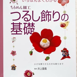 May include: A book titled "Ichiban Yoku Wakaru Chirimen Saiku: Tsurushi Kazari no Kiso" with a white background and colorful illustrations of Japanese hanging ornaments. The book cover features a red camellia flower, a white bird, and a pink cherry blossom.