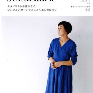 May include: A woman wearing a royal blue wrap dress with long sleeves. The dress has a V-neckline and a flowing skirt. The text "KANA'S STANDARD II" is at the top of the image. The text "スタイリスト佐藤かなの シンプルバターンでとことん楽しむ服作り" is below the title. The text "7・9・11・13号の縫い代つき 実物大パターン2枚 文化出版局" is at the bottom of the image.