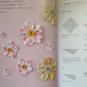 May include: A step-by-step guide on how to fold origami cherry blossoms. The instructions are written in Japanese. The image shows a close-up of the folded paper flowers, with the finished product on the left and the folding steps on the right. The flowers are made from pink and yellow paper with white polka dots.