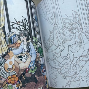 May include: An open colouring book featuring two side-by-side illustrations of a cosy room. One page is fully coloured with warm tones, showing a person sitting with a cat, books, and fruit. The other page is a black and white line art outline.
