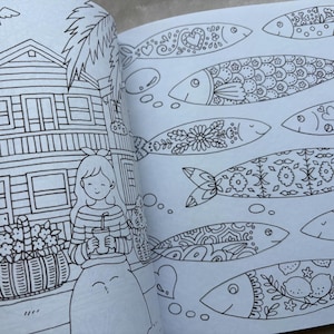 May include: An open coloring book page with detailed black and white illustrations. One page features a house, a girl holding a drink, and a dog. The other page displays several fish with intricate patterns, including hearts, flowers, and geometric designs.