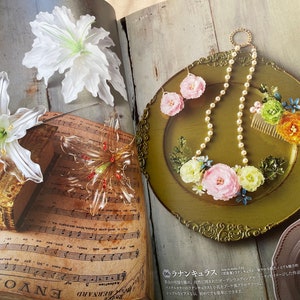May include: A close-up of a book with sheet music and three floral hair clips. The hair clips are made of clear plastic and have a delicate, floral design. The book is open to a page with sheet music and the words "ENVOI DE" are visible. The hair clips are arranged on the book in a decorative manner.