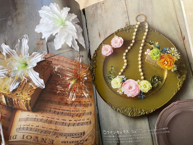 May include: A close-up of a book with sheet music and three floral hair clips. The hair clips are made of clear plastic and have a delicate, floral design. The book is open to a page with sheet music and the words "ENVOI DE" are visible. The hair clips are arranged on the book in a decorative manner.