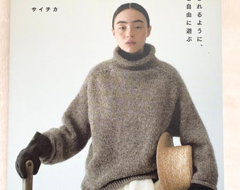 May include: A book cover with a woman wearing a brown knit sweater, white pants, and a straw hat. The book title is "Nomad's Knit" in Japanese. The book cover is light blue with white text.